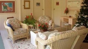 A cozy living room with wicker furniture, a small table with a vase of flowers, and a Christmas tree. - Hale-hoola B & B (Captain Cook)