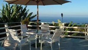 An outdoor seating area with a table and chairs, a large umbrella, and a view of the ocean. - Hale-hoola B & B (Captain Cook)