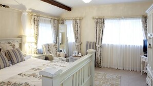 Quarto com cama, mesas de cabeceira, cômoda, televisão e cortinas.