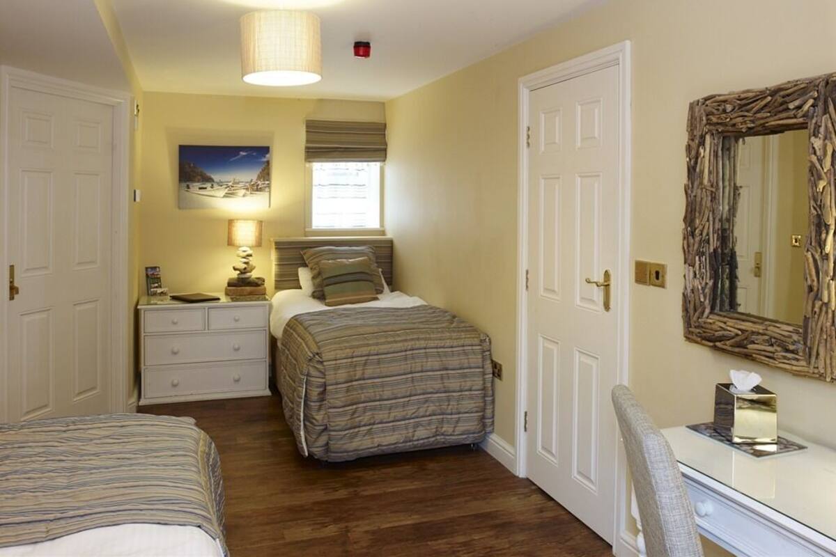 Een slaapkamer met twee bedden, een nachtkastje met een lamp, een dressoir, een spiegel en een raam met jaloezieën.