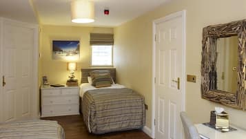 A bedroom with two beds, a bedside table with a lamp, a dresser, a mirror, and a window with blinds.