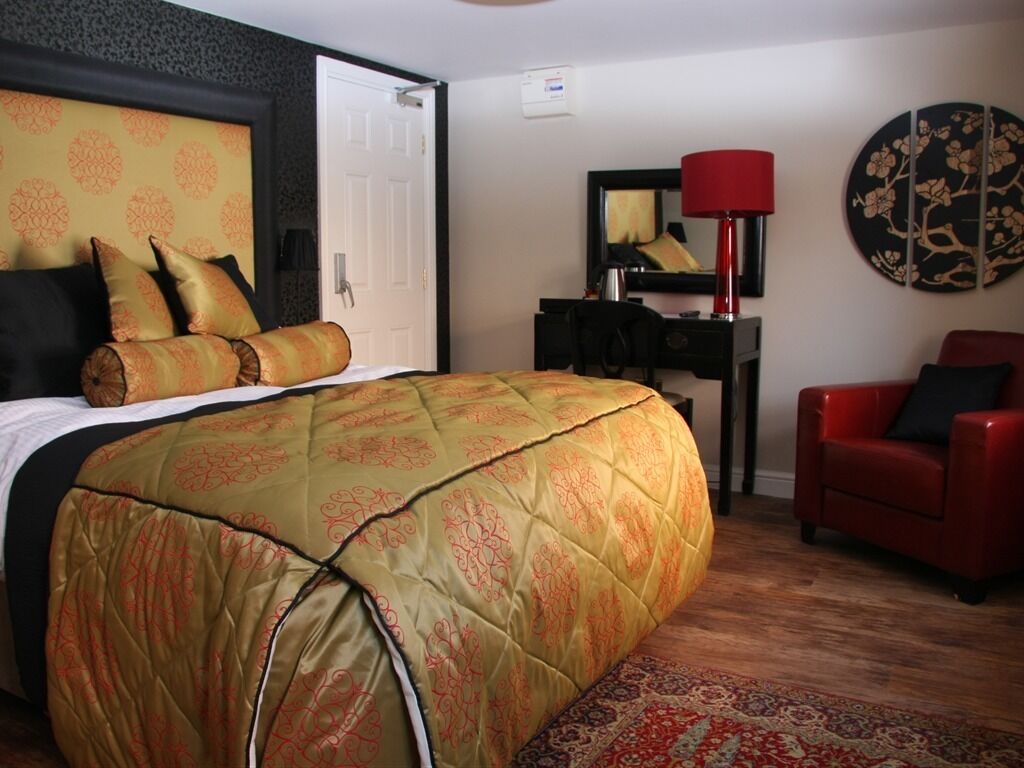 A hotel room with a large bed, a desk with a lamp, a red chair, and a decorative wall piece.