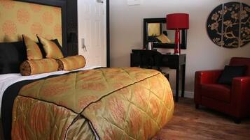 A hotel room with a large bed, a desk with a lamp, a red chair, and a decorative wall piece.