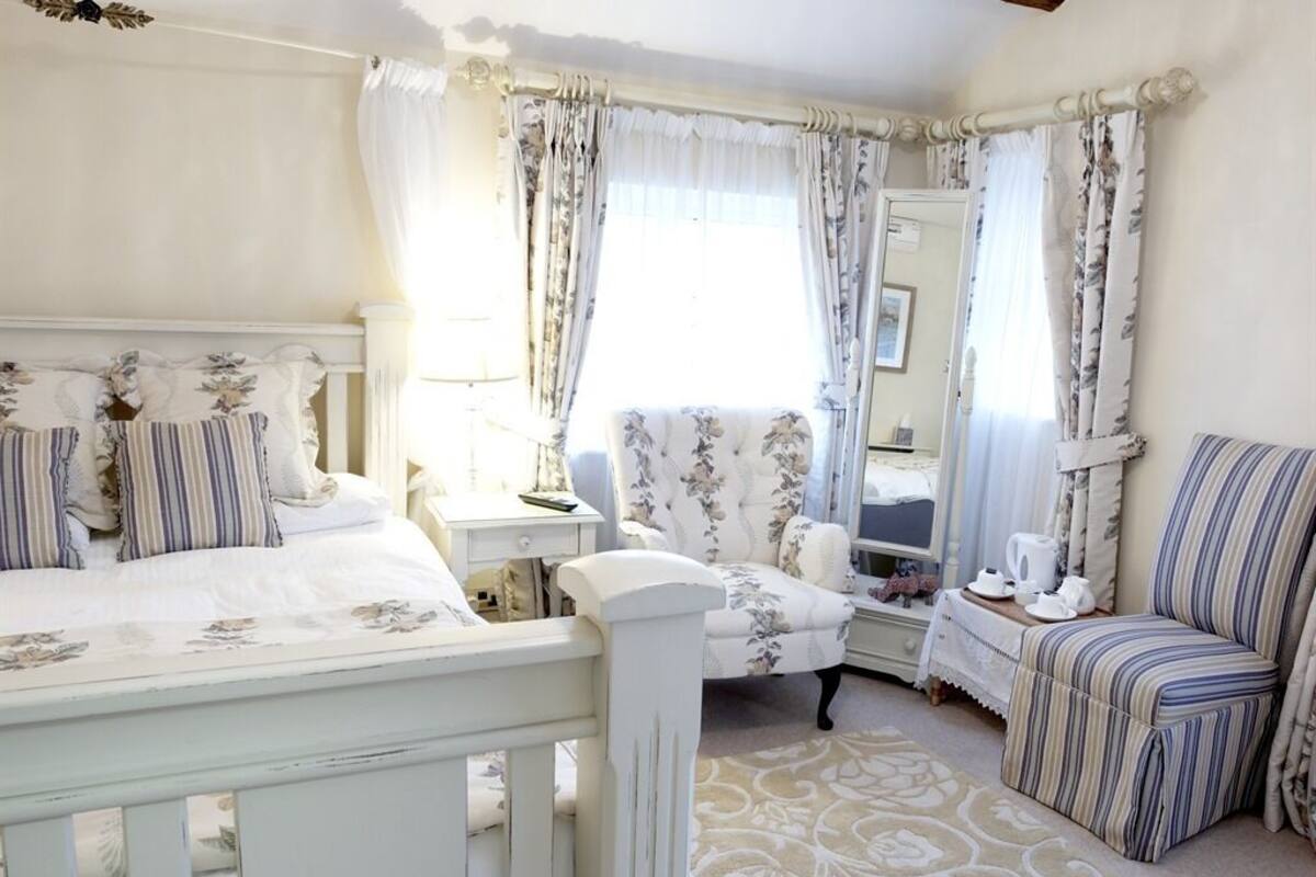 Een slaapkamer met een bed, een stoel, een nachtkastje en een raam met gordijnen.