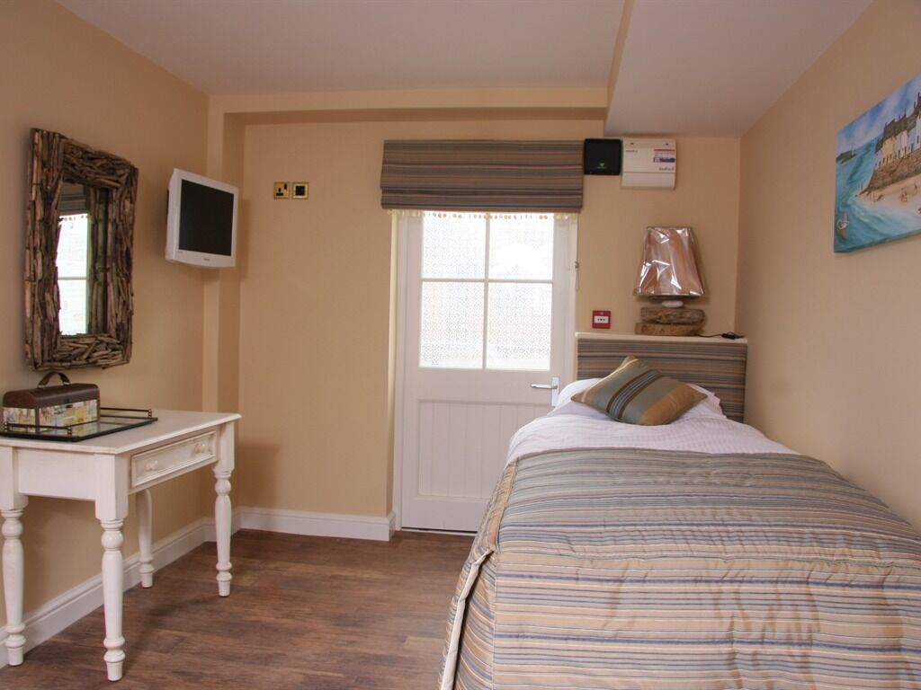 Un dormitorio con cama, escritorio, televisor, ventana y un cuadro en la pared.