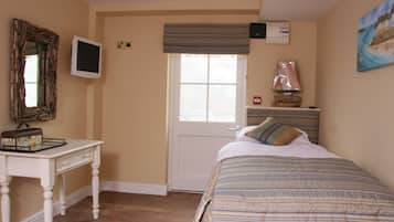 A bedroom with a bed, a desk, a television, a window, and a painting on the wall.