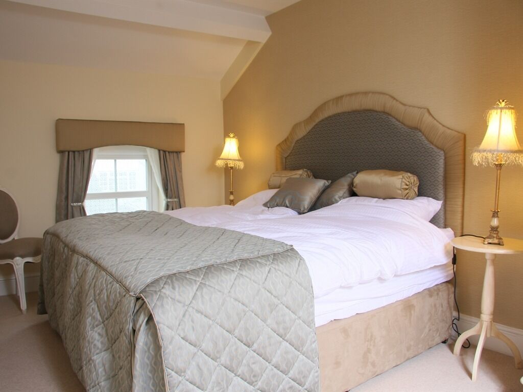 A bedroom with a large bed, two bedside lamps, a chair, and a window with curtains.