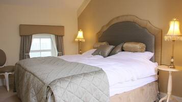 A bedroom with a large bed, two bedside lamps, a chair, and a window with curtains.