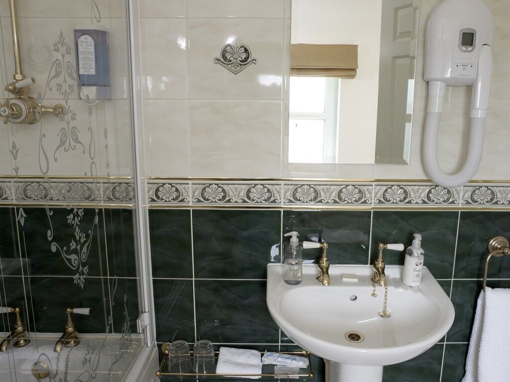 A bathroom with a white sink, two faucets, a glass shower enclosure, and a towel rack.