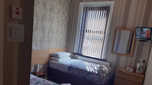 A hotel room with a bed, a bedside table, a dresser, a mirror, a window with blinds, and a TV on the wall. - Wellington Hotel (Blackpool)
