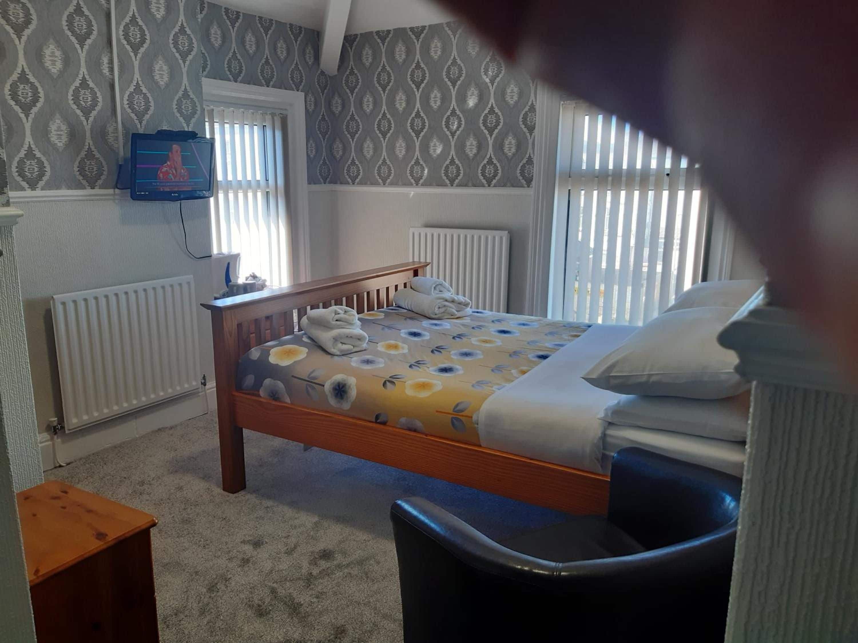 A bedroom with a wooden bed, a small bedside table, a chair, a radiator, and a television on the wall.