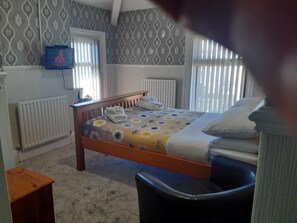 A bedroom with a wooden bed, a small bedside table, a chair, a radiator, and a television on the wall. - Wellington Hotel (Blackpool)