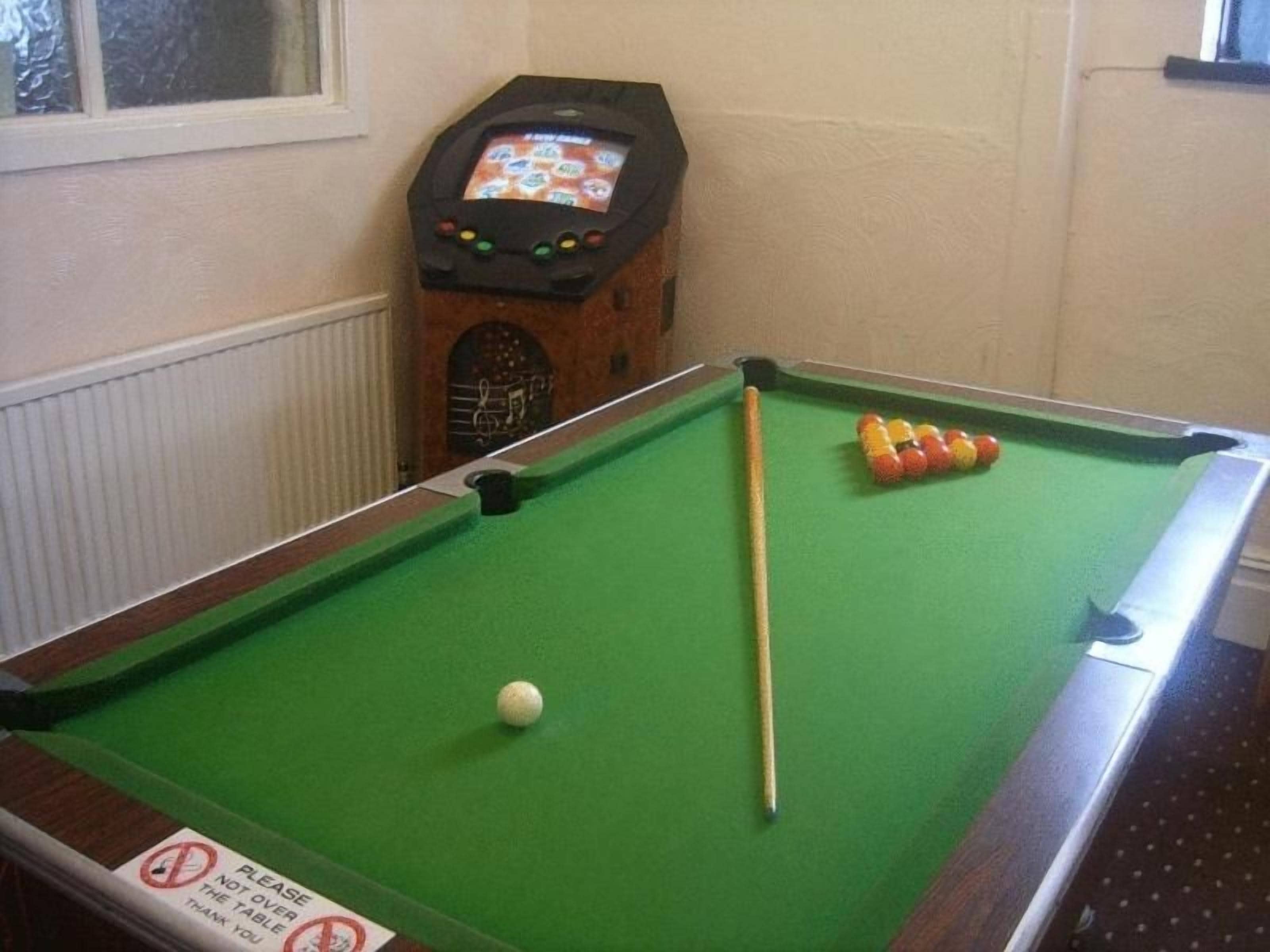 A pool table with a cue stick and balls, a pool table cover, and a pool table sign.