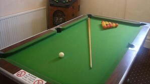 A pool table with a cue stick and balls, a pool table cover, and a pool table sign. - Wellington Hotel (Blackpool)