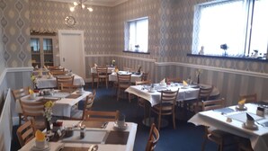 A dining area with multiple tables and chairs, patterned wallpaper, and a chandelier. - Wellington Hotel (Blackpool)