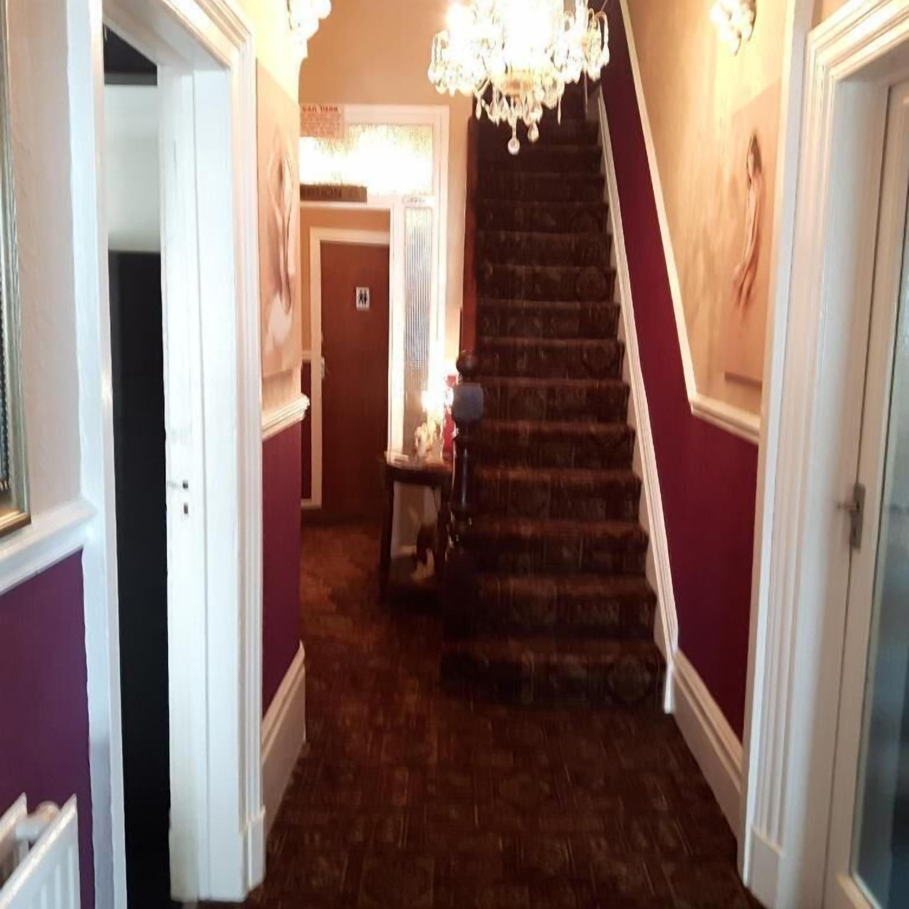 A staircase with a chandelier, a wooden floor, and a door with a sign.