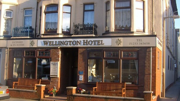A two-story Wellington Hotel with a classic facade, large windows, and a signboard displaying the name and contact number. - Wellington Hotel (Blackpool)