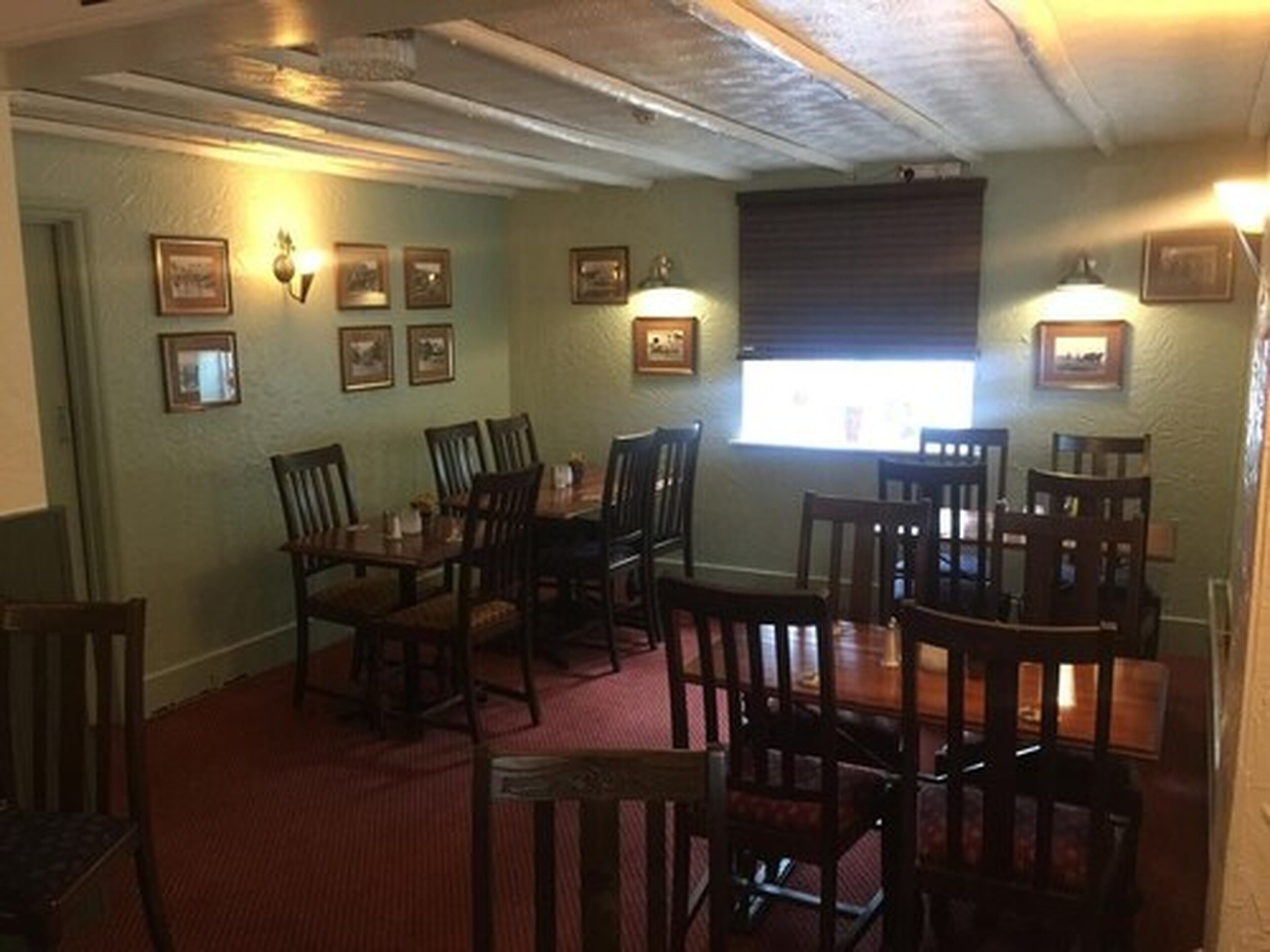 A dining area with wooden tables and chairs, framed pictures on the walls, and a window with blinds.