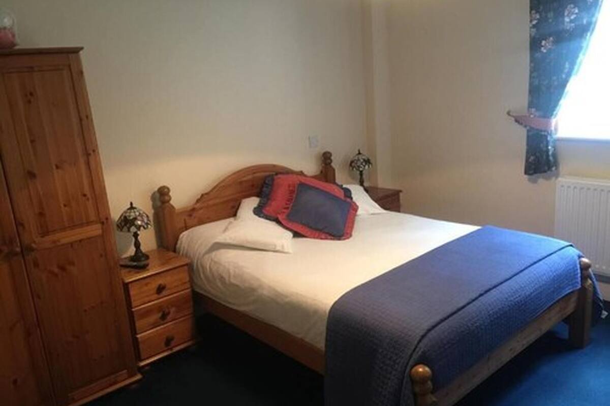 A bedroom with a wooden bed, a nightstand, a dresser, and a window with curtains.