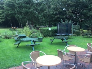 Un espace extérieur aménagé en terrasse, avec des tables et des chaises pour pique-niquer, entouré d’une végétation luxuriante et d’arbres.