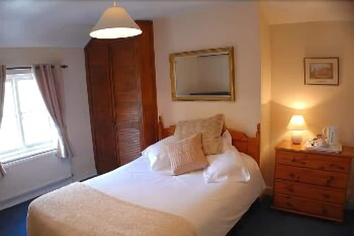 A bedroom with a bed, a wooden dresser, a mirror, and a window with curtains.