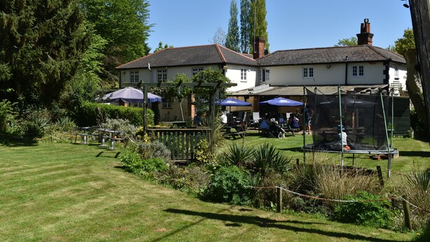 A garden with a lawn, a gazebo, and a building with a white facade and red roof. - The Winchfield Inn (Hook)