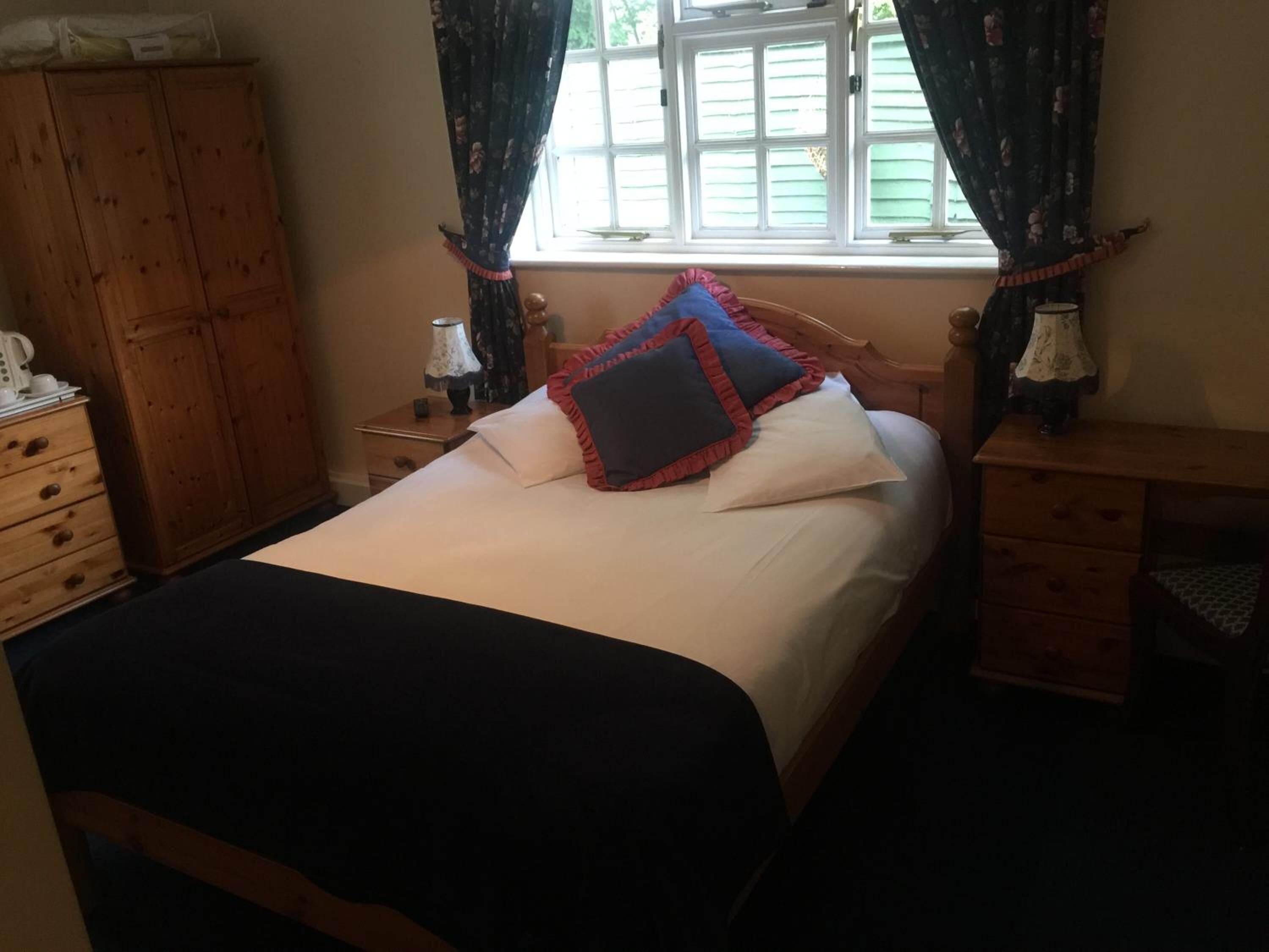 A bedroom with a bed, wooden wardrobe, nightstands, and a window with curtains.