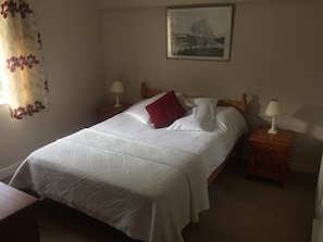 Un lit bien fait, recouvert d’une couvre-lit à motifs, deux tables de chevet avec des lampes et un tableau encadré au mur.