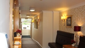 A hallway with a sofa, a table with a lamp, and a vase with flowers.
