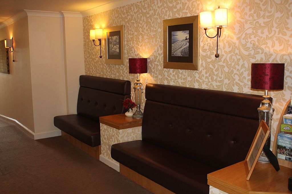 Un vestíbulo de hotel con dos sofás marrón oscuro, papel tapiz estampado, lámparas de pared e imágenes enmarcadas.