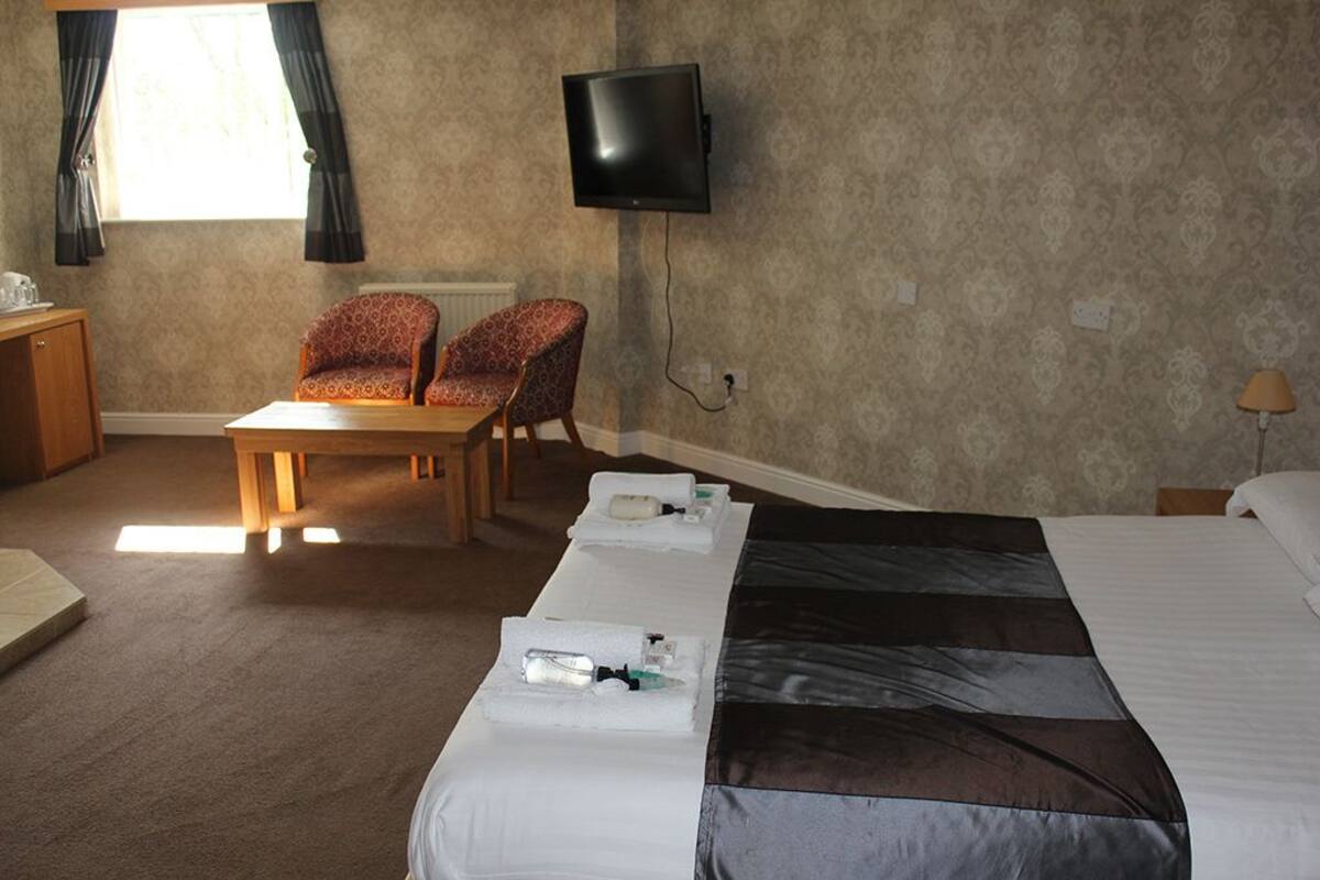 Ein Hotelzimmer mit Bett, Schreibtisch, zwei Stühlen, Fernseher und einem Fenster mit Vorhängen.