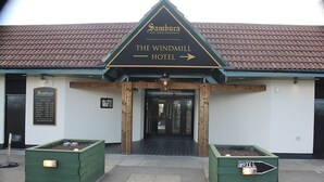 The Windmill Hotel entrance with a signboard, wooden pillars, and two green planters.