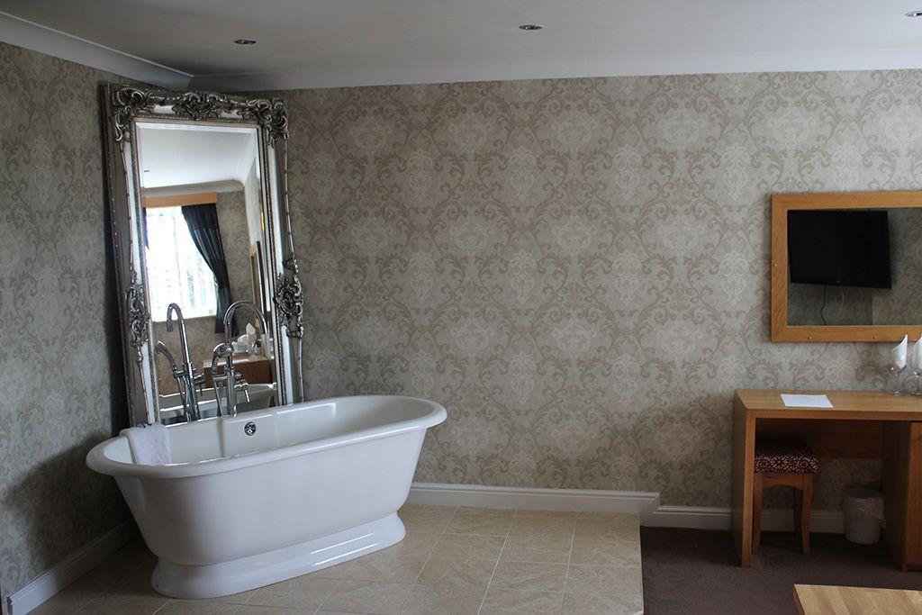 A bathroom with a freestanding bathtub, a large mirror, a wooden vanity, and a television mounted on the wall.