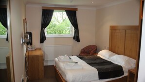 A bedroom with a wooden bed, a bedside table, a chair, a window with curtains, and a radiator.
