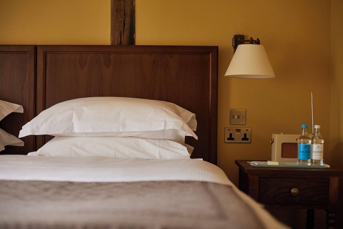 A neatly made bed with white linens, a wooden headboard, a bedside table with a lamp, and two bottles of water.