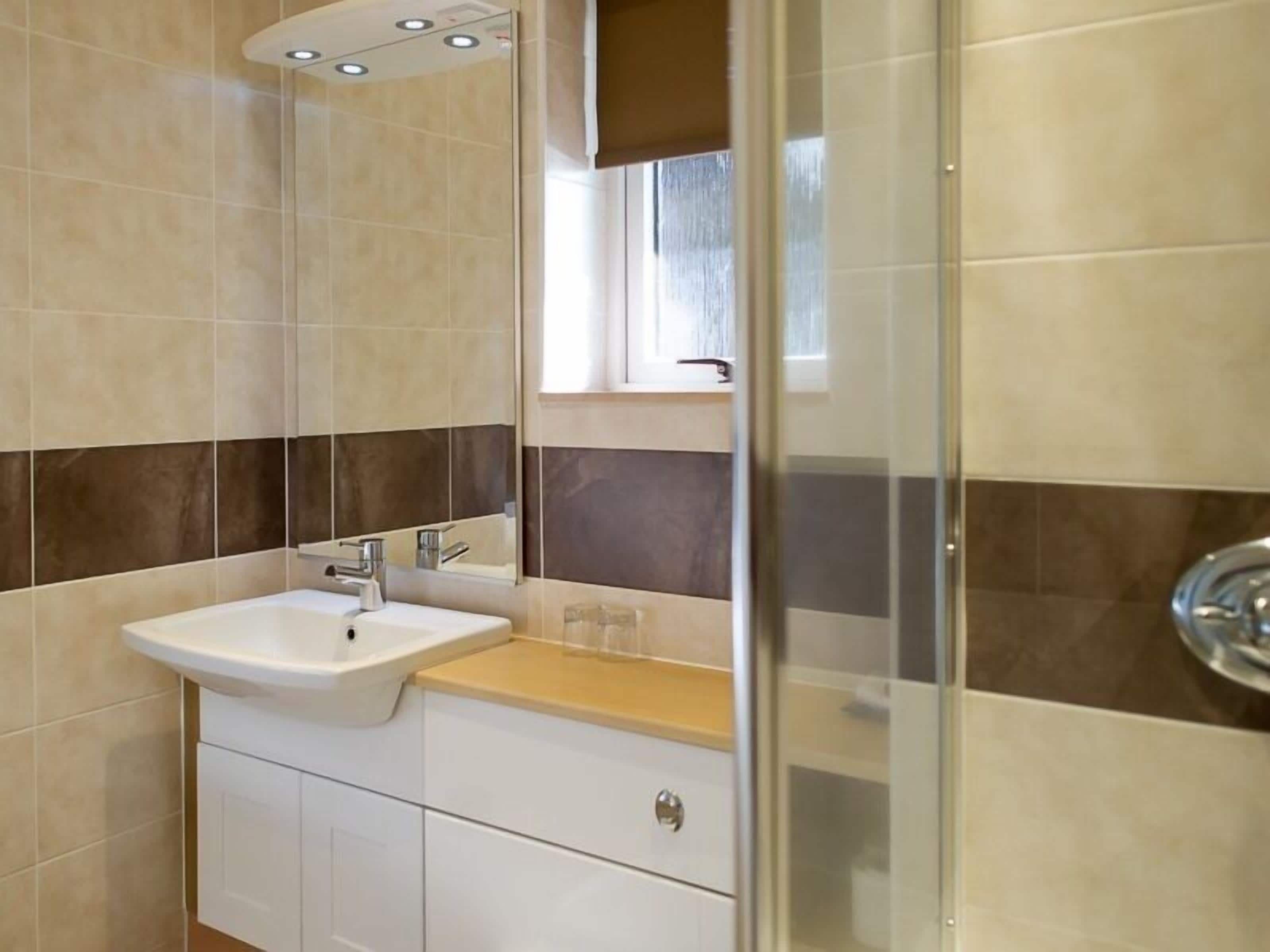 Un baño moderno con un lavabo blanco, un espejo y una zona de ducha.