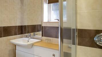 Un baño moderno con un lavabo blanco, un espejo y una zona de ducha.