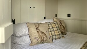 Un dormitorio con cama, dos almohadas con diseños de conejos, una lámpara de pared y un armario blanco.