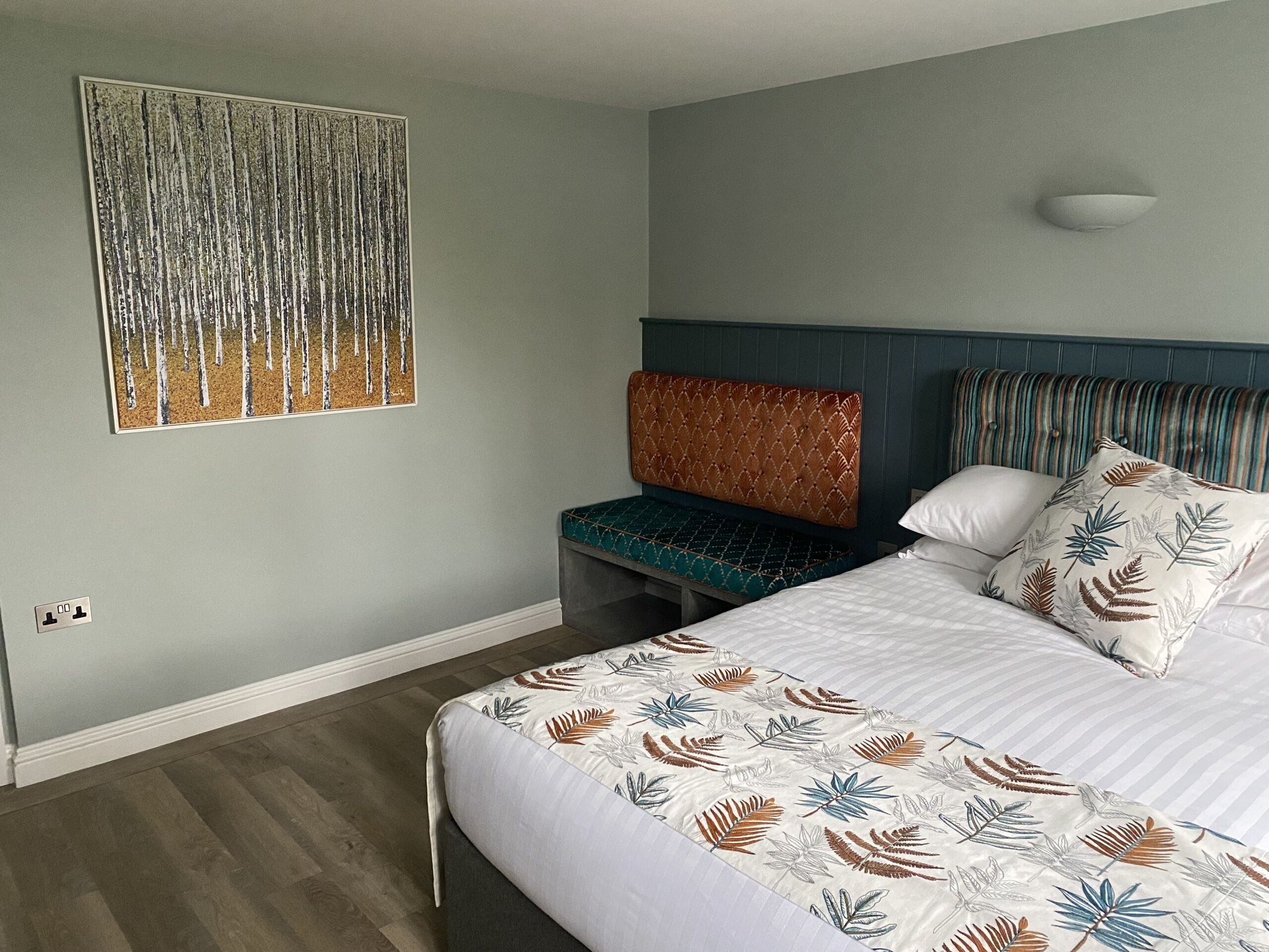 Quarto de hotel com uma cama, um banco e uma obra de arte na parede.