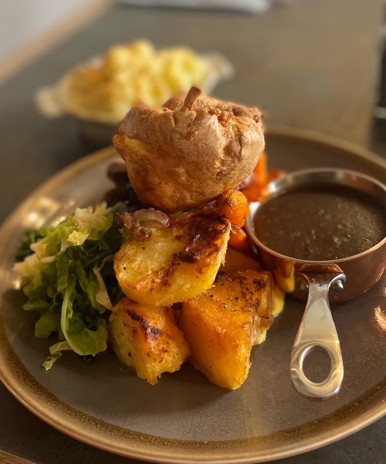 Un plato con papas asadas, un pudín yorkshire y un recipiente pequeño con salsa de carne.