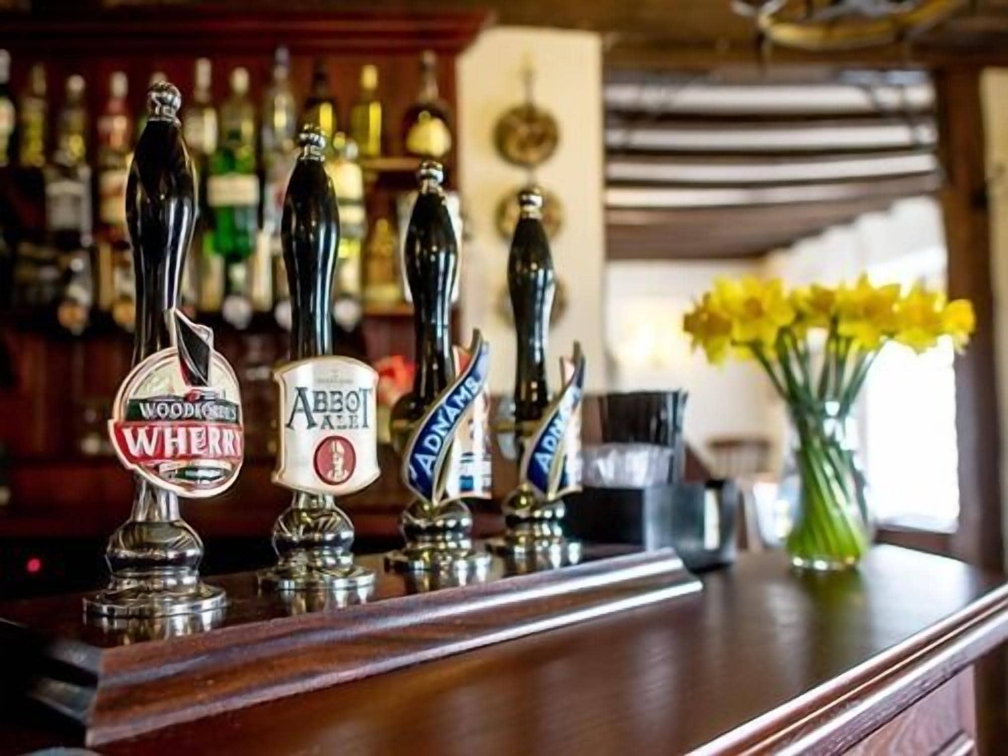 A bar with multiple beer taps, including brands like Woodies, Abbey Ale, and Adnams.