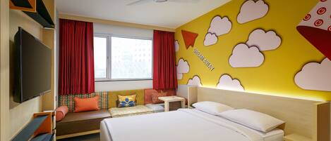 A hotel room with a bed, a TV, a desk, and a window with curtains.