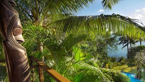 A tropical outdoor area with a pool, palm trees, and a wooden fence.
