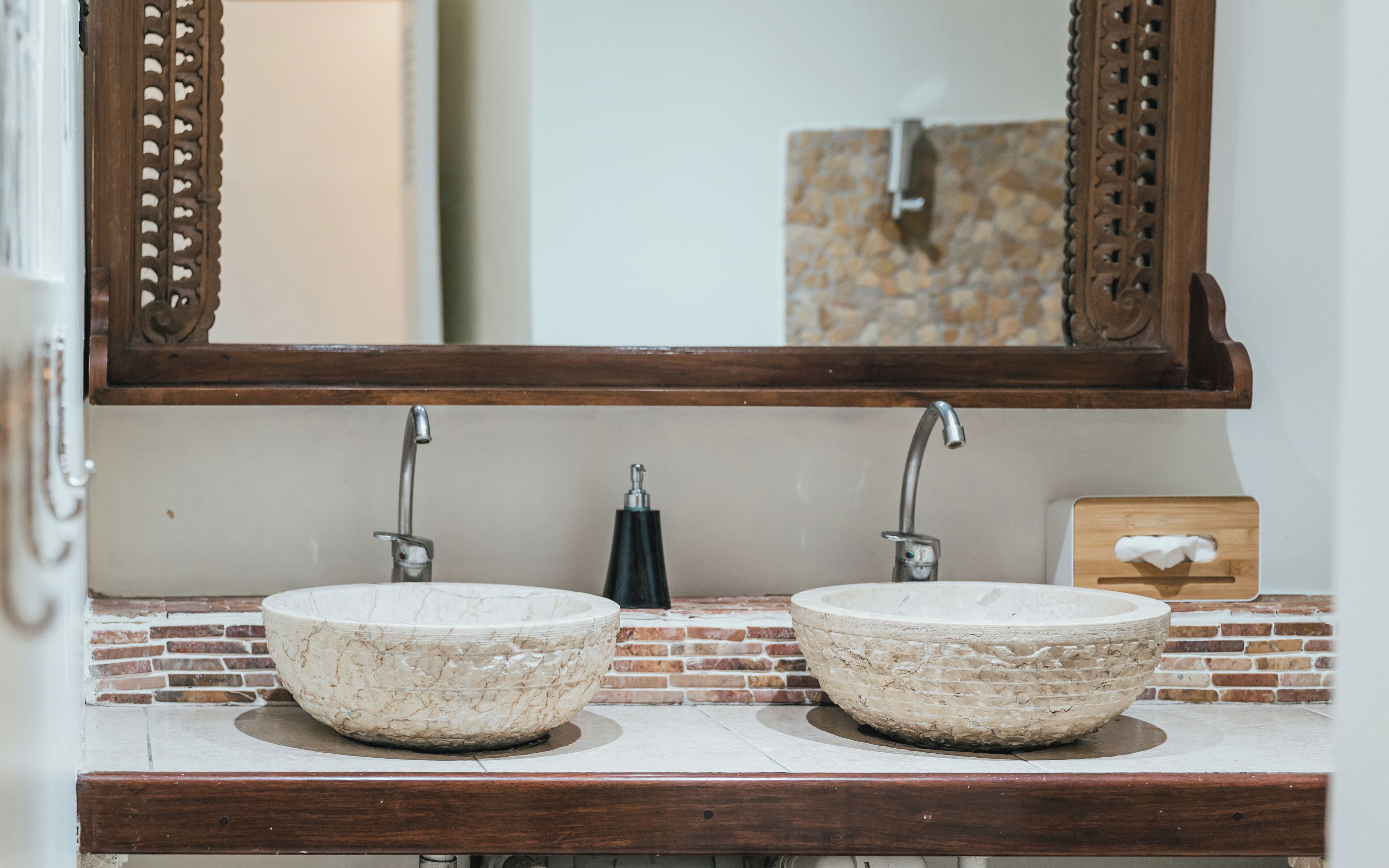 A bathroom with two stone sinks, a wooden vanity, and a mirror above.
