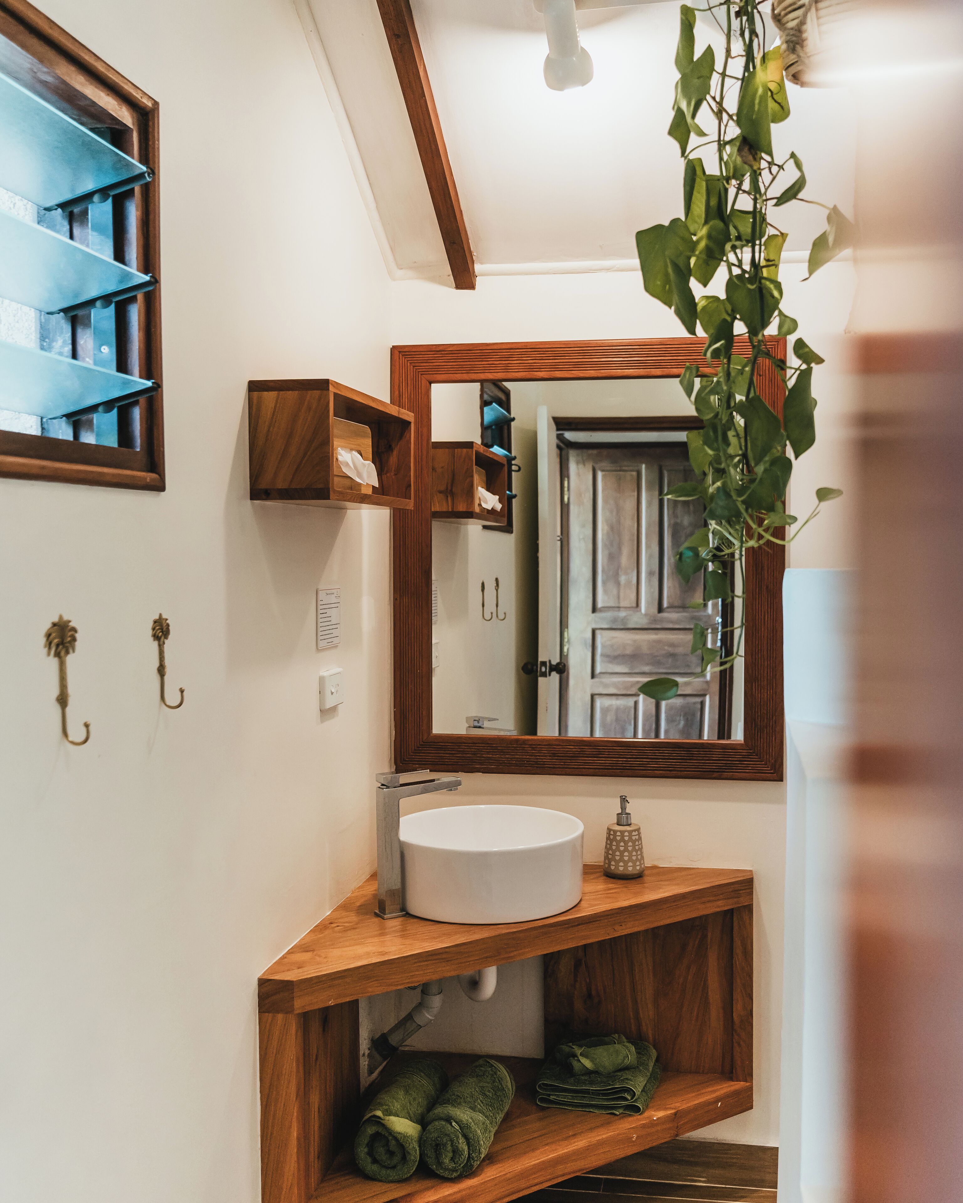 Ein Badezimmer mit einem Holzlaufschild, einem weißen Waschbecken, einem Spiegel und einer hängenden Pflanze.