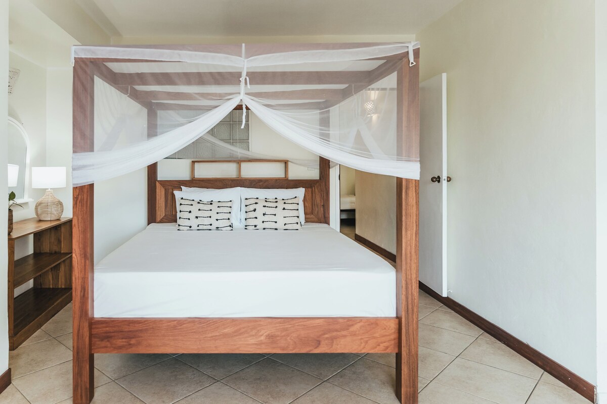 Una cama con dosel, una mesita de noche con lámpara y un espejo.