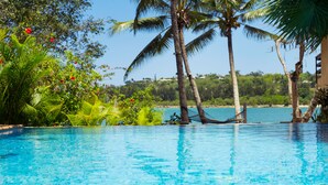 A clear blue pool with palm trees and tropical plants around it.
