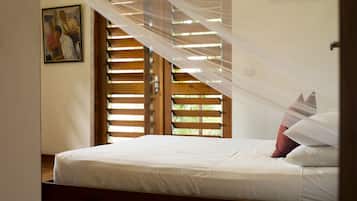 A bedroom with a bed, a window with wooden shutters, and a painting on the wall.