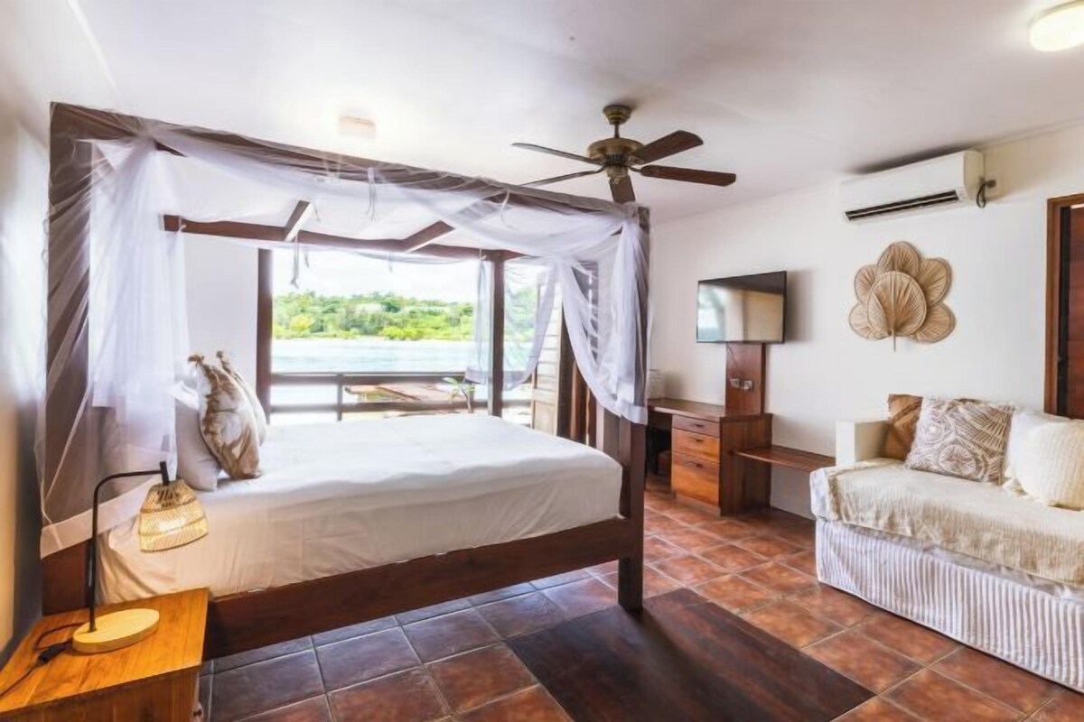 Un dormitorio con cama con dosel, ventilador de techo, televisor y vistas al exterior.