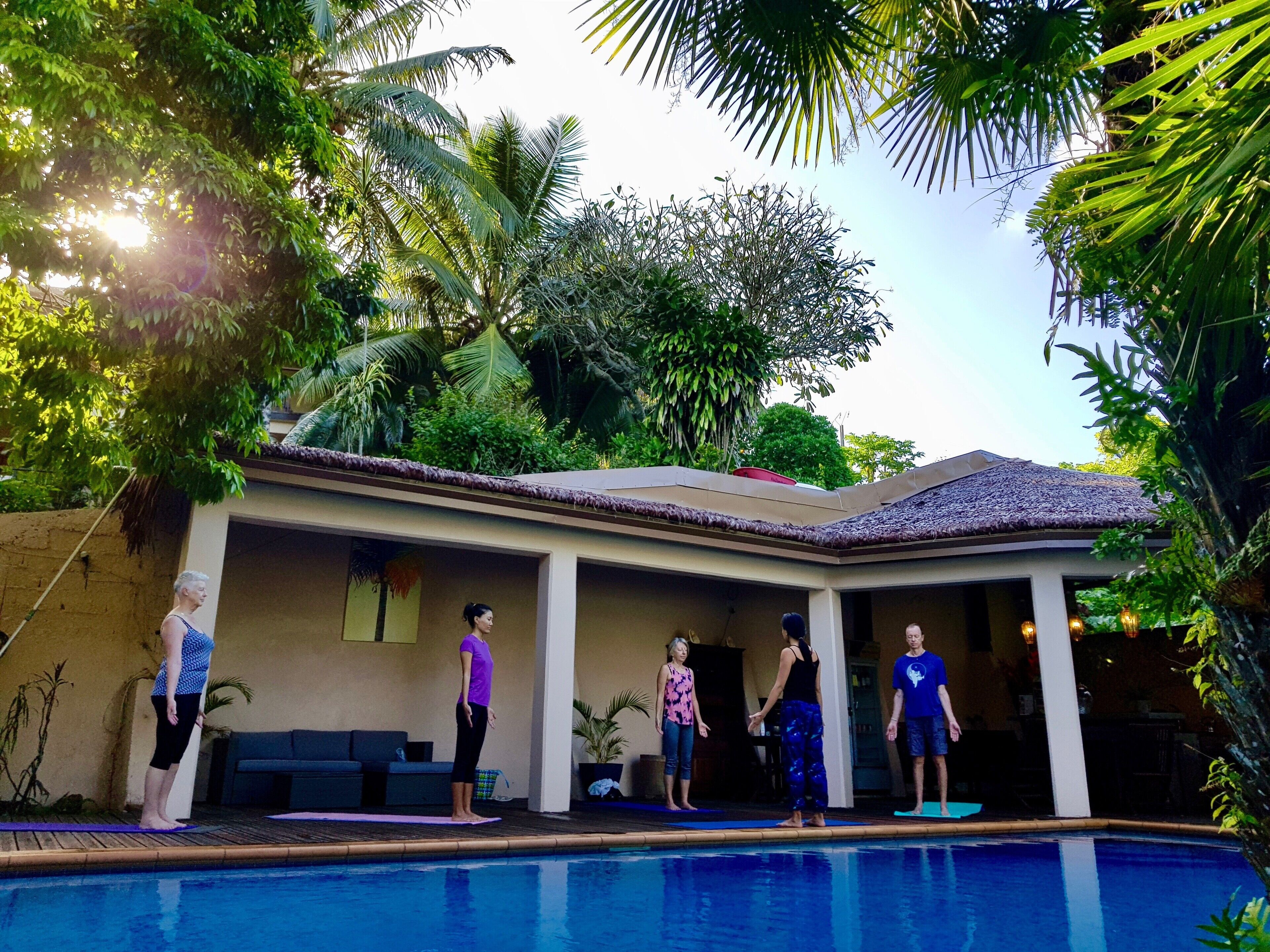 A poolside area with a covered patio, palm trees, and a clear sky.